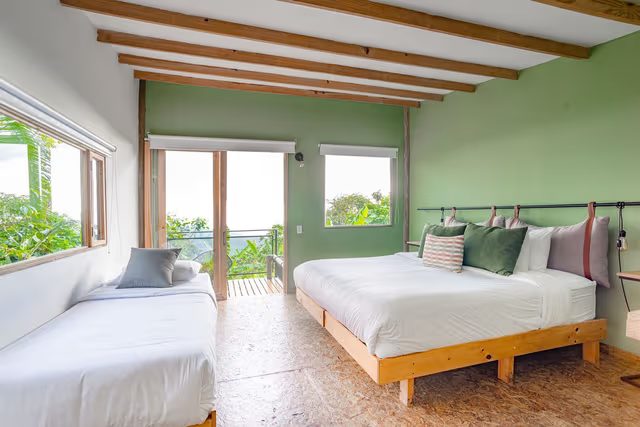 A bright room room with beds and a balcony onto the trees