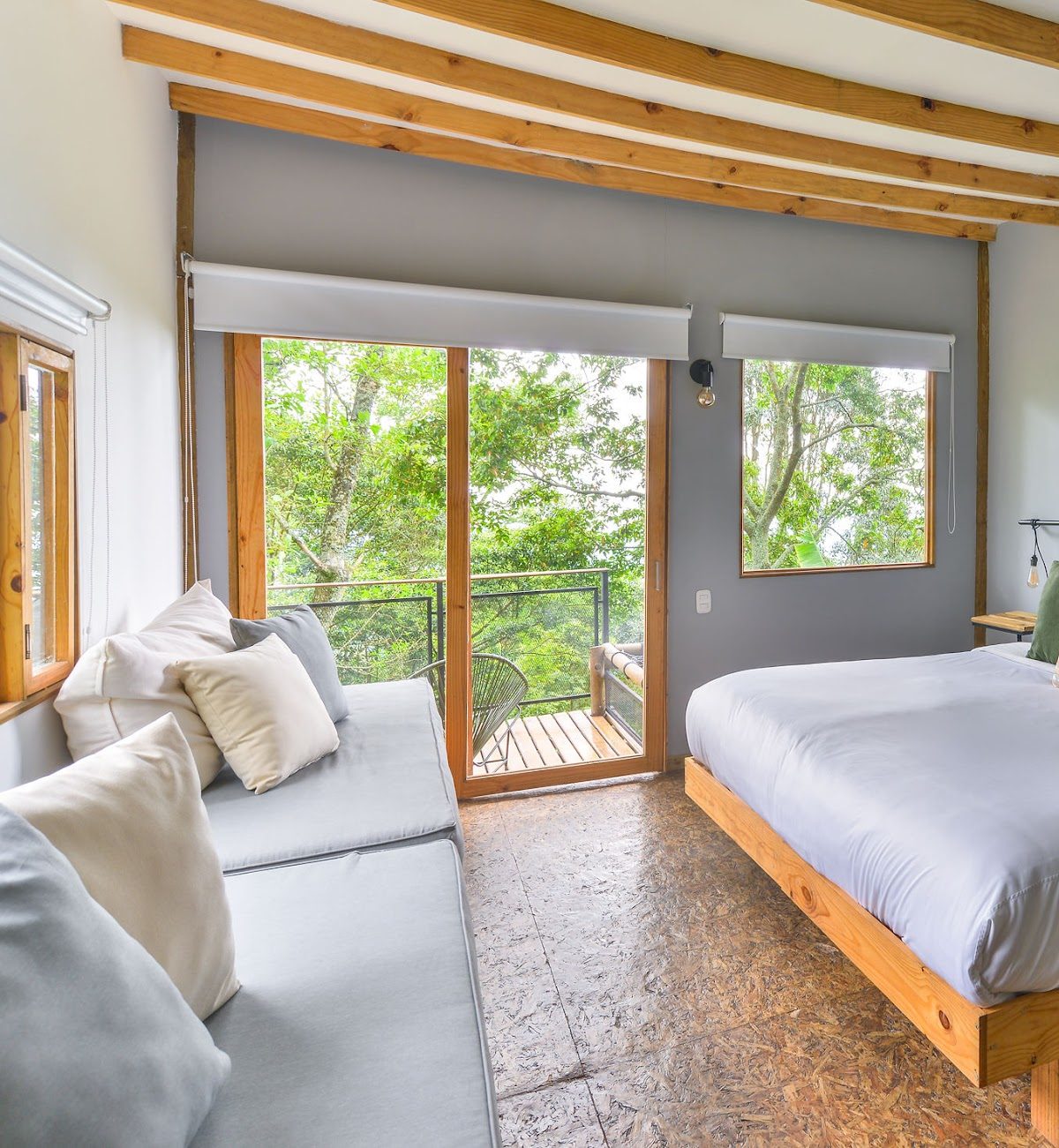 A private room with a king bed, daybed, and balcony onto the forest